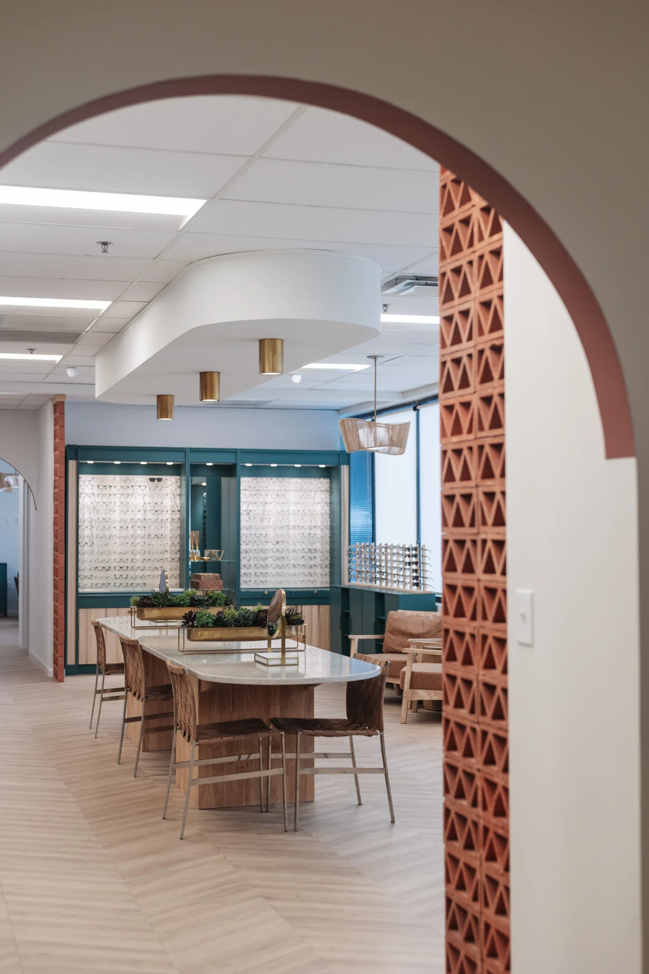 Modern optometry office interior featuring a round table with chairs, display shelves with eyeglasses, and decorative archways.
