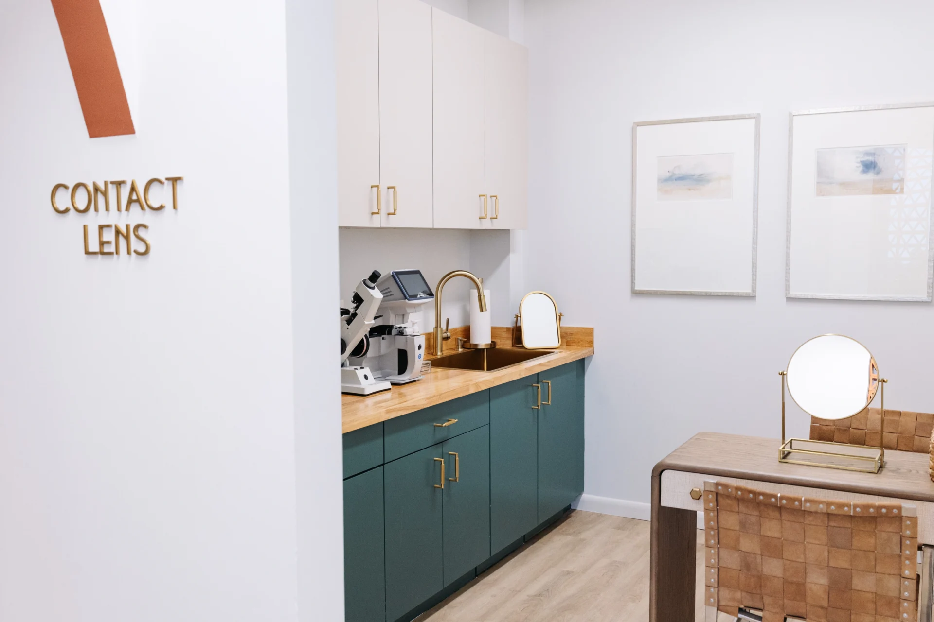 A modern optometry exam room with a countertop, medical equipment, sinks, mirrors, chairs, and a “Contact Lens” sign on the wall.