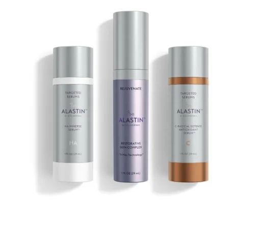 Three Alastin Skincare serum bottles—HA Immerse Serum, Restorative Skin Complex, and C-Radical Defense Antioxidant Serum—are standing upright against a white background.